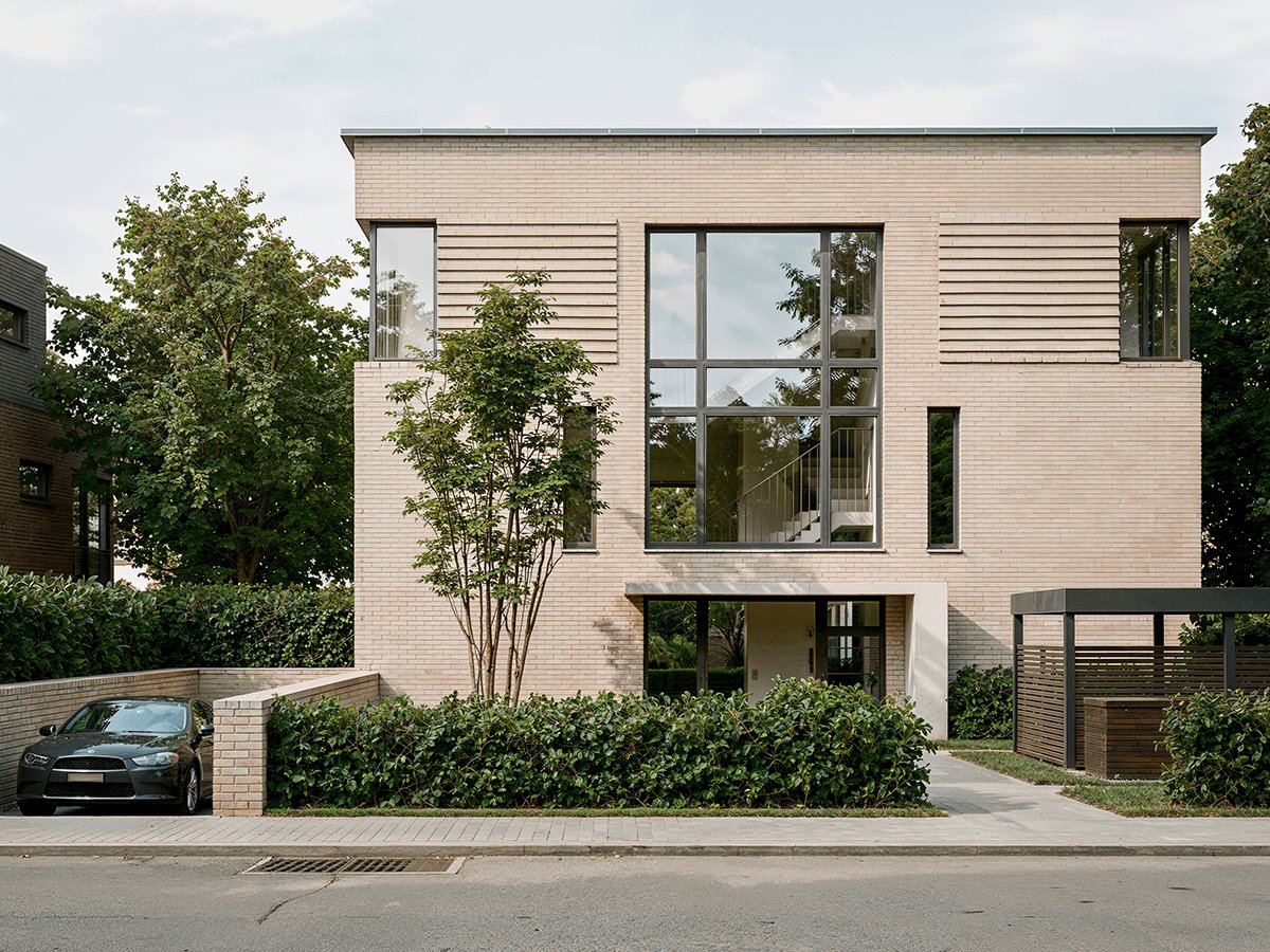 Gaia from the street: light brick building behind a hedge and front garden on Othmarscher Kirchenweg